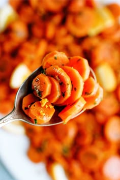 a spoon full of cooked carrots on top of a white plate with other food in the background