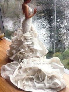 a woman standing in front of a window wearing a wedding dress with ruffles