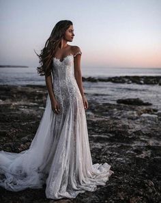 a woman standing on top of a rocky beach next to the ocean wearing a wedding dress