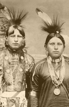 an old photo of two native american women standing next to each other with feathers on their head