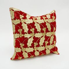 a red and gold decorative pillow on a white background with golden beads, leaves and berries