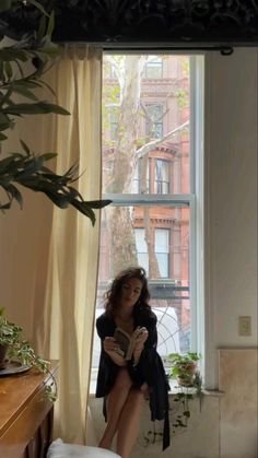 a woman sitting in front of a window reading a book