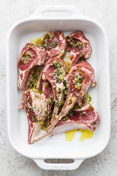 raw lamb chops in a white dish with herbs and seasoning on top, ready to be cooked