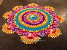 a colorful rangdi design on the ground with a lit candle in front of it