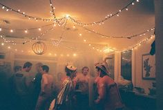 a group of people standing around each other in a room with string lights on the ceiling