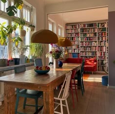 a dining room table with chairs and a bowl of fruit on it in front of a bookshelf