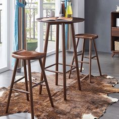 a table and two stools in a room with a cow hide rug on the floor