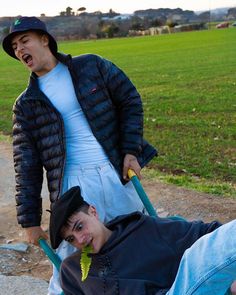 two young men are pulling a man on a wheelbarrow