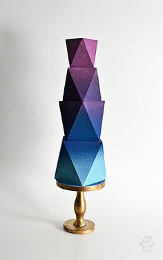 a multicolored cake sitting on top of a gold stand next to a white wall