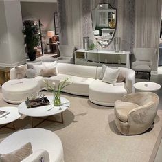 a living room filled with lots of white furniture and mirrors on the wall behind it