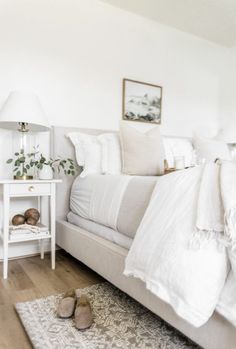 a white bed with pillows and blankets on top of it next to a night stand