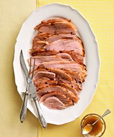 sliced ham on a white plate next to silverware and a yellow checkered tablecloth