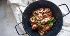 a pan filled with chicken and mushrooms on top of a white cloth next to a fork