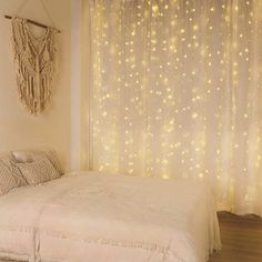 a white bed sitting under a window next to a curtain with lights all over it