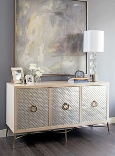 a white and gold sideboard with drawers in front of a large painting on the wall