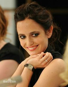 a beautiful young woman sitting at a table with her hand on her chin and smiling