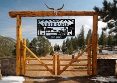 a wooden gate with a sign hanging from it's side in the middle of a dirt road