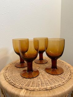 four wine glasses sitting on top of a wicker table next to a white wall