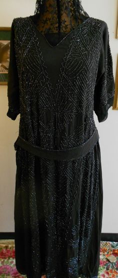 "1920's, 38\" bust, light weight black silk crepe gown entirely sewn in iridescent black glass beaded Art Deco abstract geometric design, from shoulder to hem. A matching sash edged in the same beads is attached to the gown at upper hip. Neckline of gown is open to a small V, with a modesty of black chiffon at the bottom of the V, neckline is edged with a single row of iridescent beads. The gown has short raglan sleeves, covered with the same beaded motif, edged in a narrow band of chiffon. Bodi 1920s Vintage Dresses, Percival Graves, Black Flapper Dress, 1920 Style, 1920 Dress, Black Beaded Dress, Iridescent Black, Deco Dress, Satin Wedding Gown