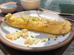 a white plate topped with an omelet next to a bowl filled with sauce