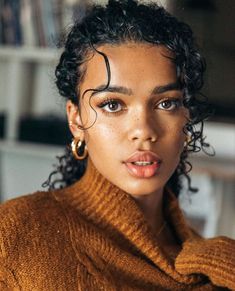 a close up of a person with curly hair wearing a brown sweater and gold hoop earrings