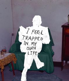 a man sitting in a chair with a sign on it that says i feel trapped in my own life