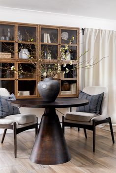 a dining room table with two chairs and a vase filled with flowers on top of it