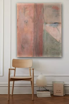 an abstract painting hangs on the wall next to a wooden chair and bookshelf