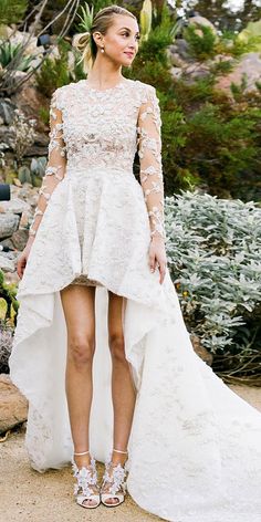 a woman standing in front of some bushes wearing a dress with high low hems