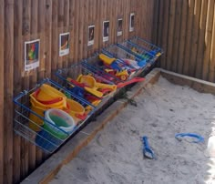 a row of beach toys sitting on top of a sand covered ground next to a wooden fence