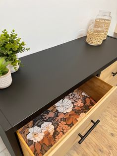 a black desk with drawers and flowers on it next to a potted green plant