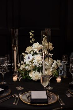 the centerpiece is surrounded by white flowers and candles on a black table cloth with gold trim