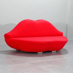 a large red couch sitting on top of a cement floor next to a white wall