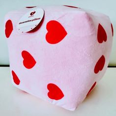 a pink and red heart shaped pillow on a white surface with a tag attached to it