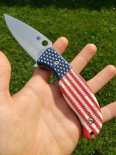 a hand holding a red, white and blue american flag pocket knife