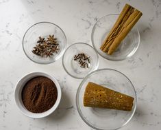 three bowls with spices and cinnamon sticks in them on a marble counter top next to other glass dishes