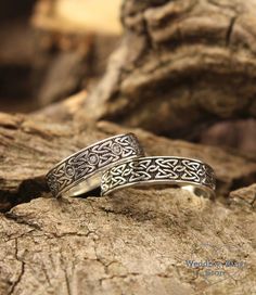 two silver rings sitting on top of a piece of wood next to a tree trunk