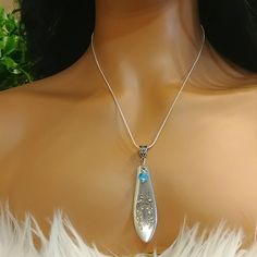 a woman wearing a silver necklace with a blue stone in the center and white feathers around it