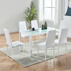 a dining room table with white chairs and a potted plant on the floor next to it