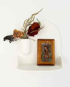 a white shelf with a painting and a flower in a vase on top of it