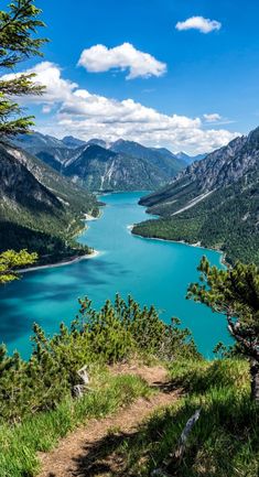 a scenic view of a lake and mountains from the top of a hill with blue water