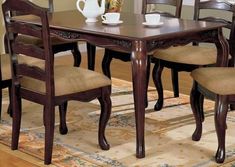 a dining room table with chairs and a vase on top of it in front of a rug