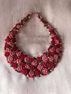 a pink and green beaded necklace on a white cloth with beads in the shape of roses