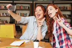 two young women sitting at a table with their hands in the air and one holding up her phone