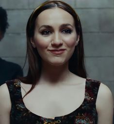 a woman with long brown hair wearing a black dress and smiling at the camera while standing in front of a brick wall