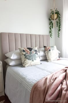 a bed with white sheets and pillows in a bedroom next to a plant hanging on the wall