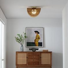 a painting hangs on the wall next to a wooden cabinet and plant in a vase