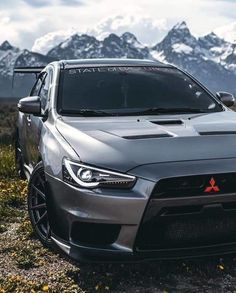 a silver car parked on top of a grass covered field next to mountains with snow capped peaks in the background