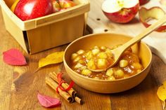 a wooden bowl filled with apples next to cinnamon sticks