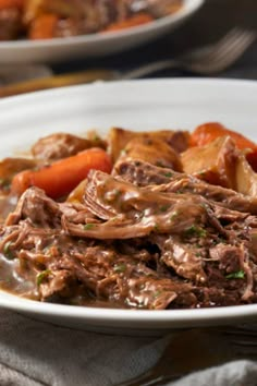 a white bowl filled with beef and carrots on top of a table next to a fork